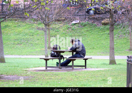 Giovane adolescente studente seduto da solo nella contemplazione al tavolo da picnic panca in parco pubblico con zaino in spalla per la società Foto Stock