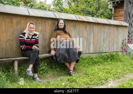 Due donne sedute su una panca in legno su una piccola strada di campagna nella regione Maramures, Romania Foto Stock