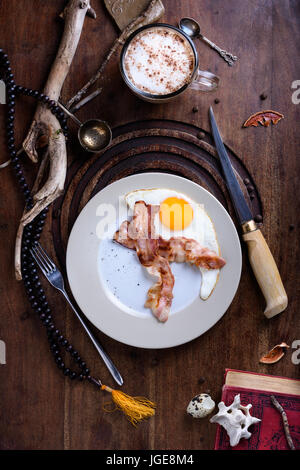 La prima colazione di pancetta e uova fritte con latte il caffè sul tavolo antico. Cacciatori vintage stile capanna. Vista dall'alto. Foto Stock