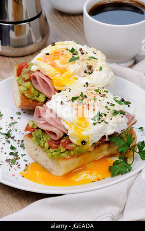 Le uova in camicia con avocado, pomodori, fette di prosciutto su una baguette per colazione Foto Stock