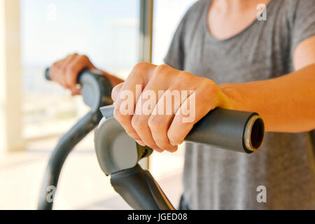 Primo piano di un giovane uomo caucasico in grigio di una t-shirt utilizzando un trainer ellittico Foto Stock