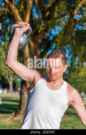 Primo piano di montare l'uomo muscolare il sollevamento di un carico pesante kettlebell nel parco all'aperto Foto Stock