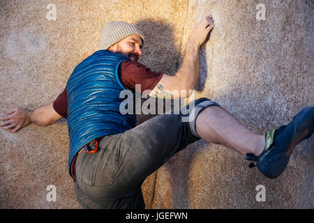 Giovane uomo caucasico con barba salite di roccia nel deserto con nessuna attrezzatura di sicurezza Foto Stock