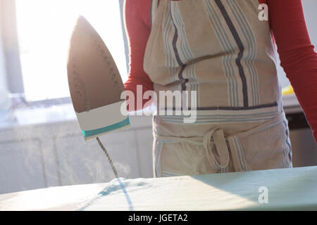 La sezione centrale della donna maglietta di stiratura sulla tavola da stiro in cucina a casa Foto Stock