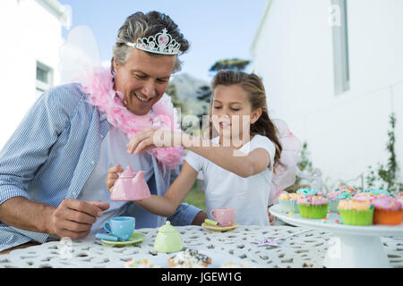 Sorridente padre e figlia in fairy costume avente un tea party in giardino Foto Stock