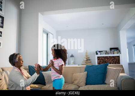 Sorridente nipote e nonna giocando battimani giochi sul divano nel soggiorno di casa Foto Stock