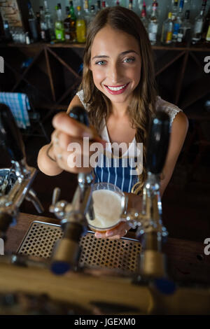 Ritratto di bella barista versare birra dal rubinetto in vetro al ristorante Foto Stock