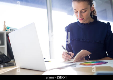 Executive femmina iscritto nel diario alla sua scrivania in ufficio Foto Stock
