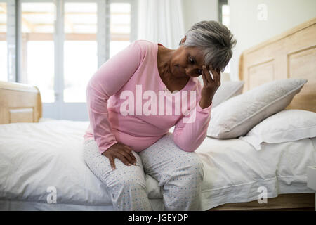 Tense senior donna seduta sul letto in camera da letto a casa Foto Stock