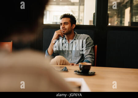Bel giovane uomo seduto al tavolo della sala conferenze e di ascolto a un collega. L'uomo durante la riunione di affari. Foto Stock