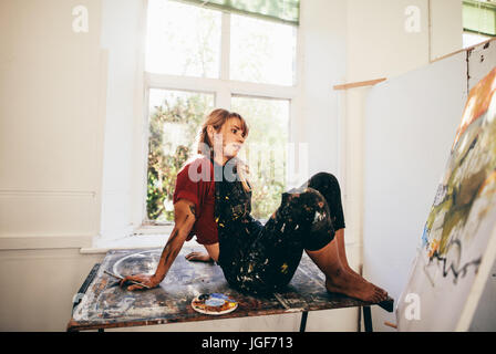 Tiro al coperto del pittore femmina lavora in studio. Rilassata giovane donna artista guardando la pittura nella sua officina e pensare. Foto Stock