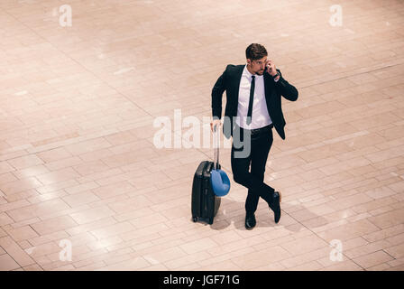 Vista Top Shot del giovane imprenditore permanente al terminal aeroportuale con la valigia e parlando al telefono. Viaggiatori di affari una telefonata mentre waitin Foto Stock