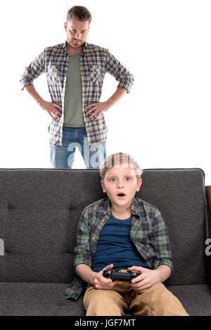 Padre serio con le mani sulla vita guardando il Figlio seduto sul divano con il joystick, problemi familiari concetto Foto Stock