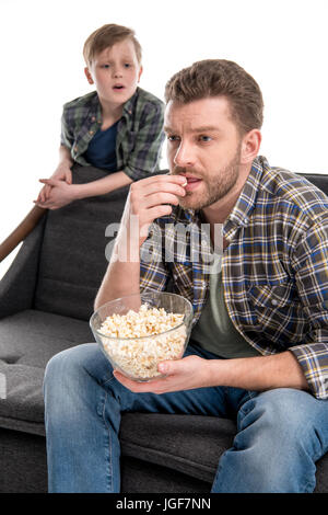 Figlio di parlare con padre seduto sul divano e mangiare popcorn dal recipiente, problemi familiari concetto Foto Stock