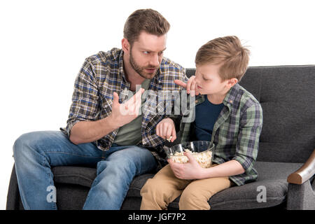Padre di parlare con il Figlio seduto sul divano e mangiare popcorn dal recipiente, problemi familiari concetto Foto Stock