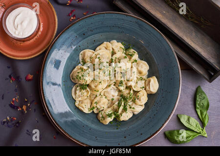 Vista ravvicinata di bollito in casa gnocco di carne servita in creta blue plate con salsa cremosa. Composizione in stile rustico su sfondo di legno Foto Stock