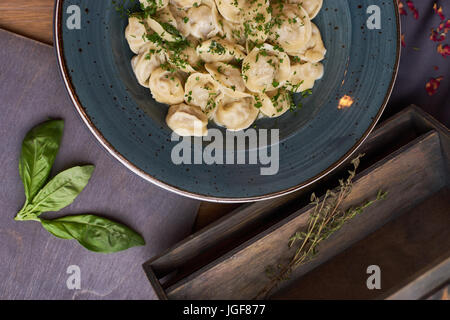 Vista ravvicinata di bollito in casa gnocco di carne servita in creta blue plate con salsa cremosa. Composizione in stile rustico su sfondo di legno Foto Stock