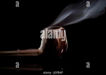 Accesa al fumo di tabacco tubo di vetro riflettente superficie, con lo spostamento di fumo, chiave di basso sfondo nero Foto Stock