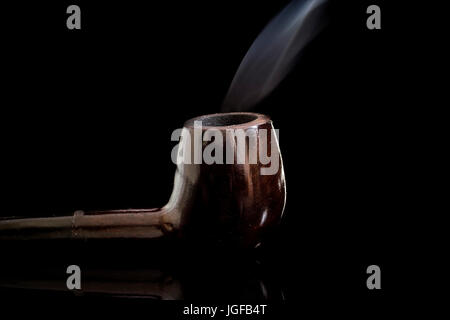 Accesa al fumo di tabacco tubo di vetro riflettente superficie, con lo spostamento di fumo, chiave di basso sfondo nero Foto Stock