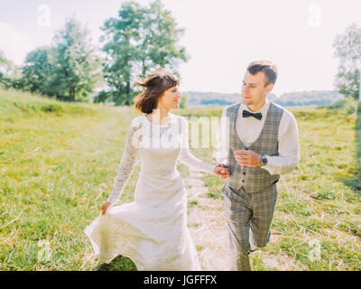 Close-up ritratto di allegro sposi tenendo le mani mentre è in esecuzione la campagna. Foto Stock
