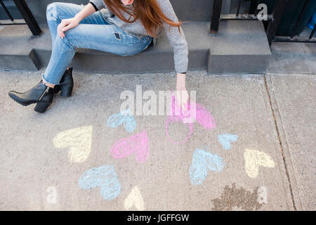 La donna caucasica disegnare cuori con un gessetto sul marciapiede Foto Stock