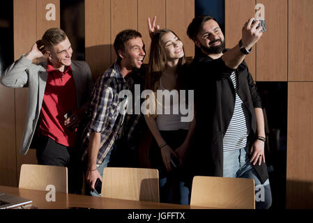 Quattro giovani in piedi in camera dalla finestra e rendendo selfie. Foto Stock