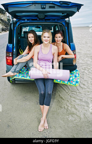 Ritratto di sorridente donne caucasici abbracciando in berlina di auto sulla spiaggia Foto Stock