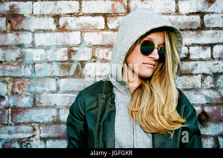 La donna caucasica indossando occhiali da sole vicino a un muro di mattoni Foto Stock
