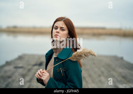 Grave donna caucasica permanente sulla dock tenendo un gambo di erba Foto Stock