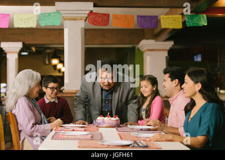 Uomo anziano soffiando le candeline sulla torta di compleanno nel ristorante Foto Stock