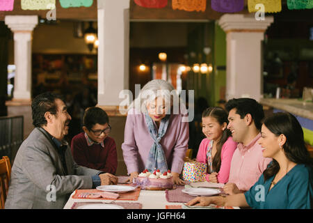 Donna anziana soffiando le candeline sulla torta di compleanno nel ristorante Foto Stock