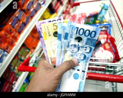 Foto di una mano azienda Philippine peso bollette, mentre all'interno di un negozio di alimentari Foto Stock