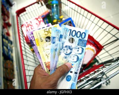 Foto di una mano azienda Philippine peso bollette, mentre all'interno di un negozio di alimentari Foto Stock