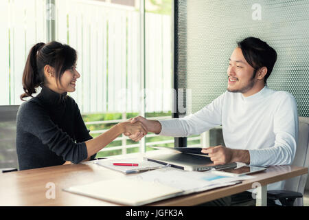 Paio di Asian business persone con abbigliamento casual parlando con felice e agitando la mano in un ufficio moderno o coffee shop. Business il concetto di successo Foto Stock