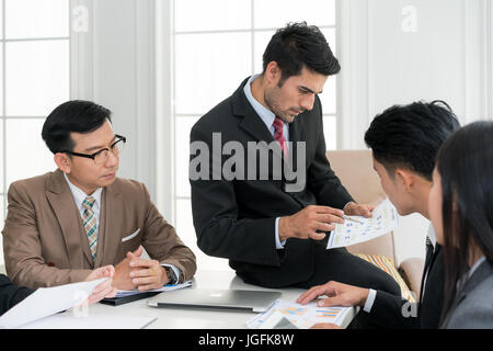 Asian smart manager spiegando riunione interna al suo team di progetto in un ufficio moderno. La multi etnico persona business group in tuta. Progetto e Busi Foto Stock