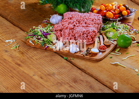 Le carni bovine macinate a crudo su tavola di legno con erbe e spezie la carne macinata con spezie Foto Stock