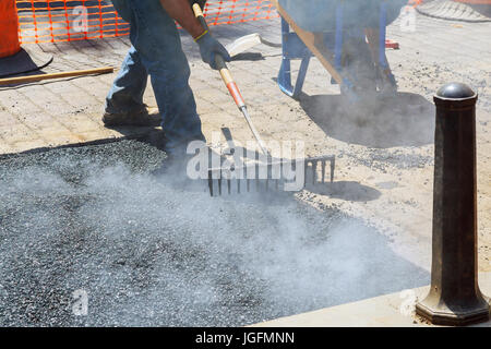 Operai edili nel corso di asfaltatura lavori stradali indossando tute. Il lavoro manuale sul sito in costruzione. Foto Stock