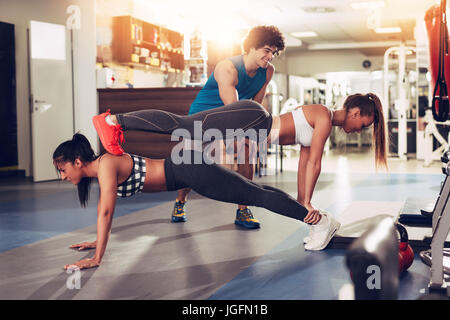Due ragazze sorridenti esercizi in palestra con personal trainer. Foto Stock