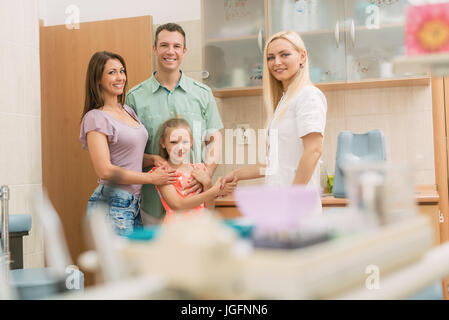 Bambina e i suoi genitori la visita dal dentista. La bambina è agitando la mano con la femmina del dentista e sorridente. Guardando alla fotocamera. Foto Stock