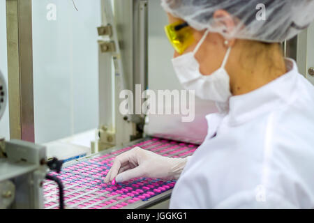 Un dipendente supervisiona il confezionamento di pillole di medici. Technolgist farmaceutica indossando indumenti di protezione. Foto Stock