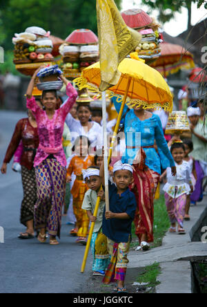 Bambini che portano ombrelloni e bandiere nel corso di un tradizionale tempio Hindu festival processione, isola di Bali, Canggu, Indonesia Foto Stock