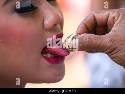 Una ragazza adolescente avente la propria lingua benedetta con un anello da un sacerdote prima di un dente il deposito di cerimonia, isola di Bali, Canggu, Indonesia Foto Stock