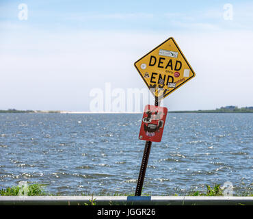 Vecchi e malandati dead end firmare alla fine di una strada con acqua dietro di essa Foto Stock