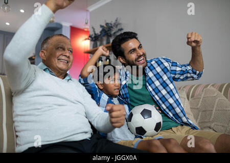 La famiglia felice con le braccia sollevate guardando la partita di calcio mentre è seduto sul divano di casa Foto Stock