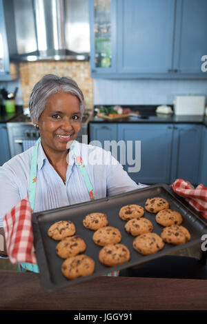 Angolo alto ritratto di donna che mostra biscotti mentre in piedi in cucina a casa Foto Stock