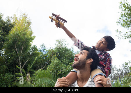 Ragazzo giocando con aereo mentre è seduto sulla spalla dei padri in cantiere Foto Stock