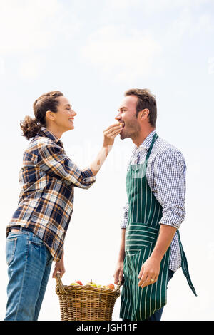 Sorridente giovane donna alimentazione di Apple per uomo contro sky Foto Stock