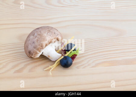 Testa a fungo di castagno, due mirtilli e foglia di lattuga sul tagliere di legno Foto Stock