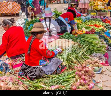 Pisac Perù mercato, locali Peruviani donne con capelli intrecciati, cappelli e indossando abiti tradizionali, vendere la verdura al mercato di Pisac, Sud America. Foto Stock