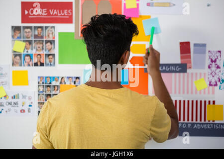 Vista posteriore del giovane uomo puntando alla nota adesiva in ufficio creativo Foto Stock